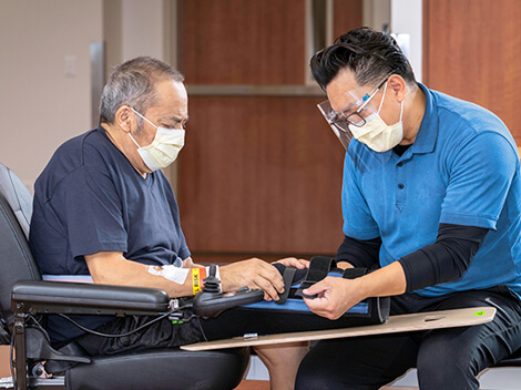 Male therapist wearing a clear plastic face cover putting a amputee cuff on a man's leg.