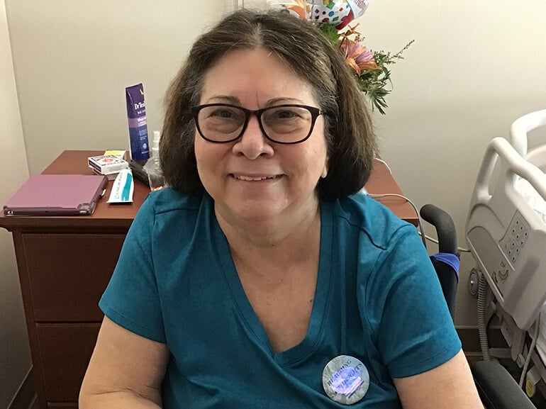 Gwendolyn smiling and wearing a teal-colored shirt while sitting in her hospital room.