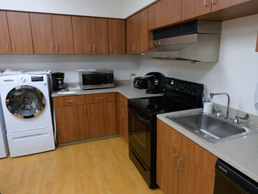 A therapy room with washer, dryer, microwave, stove and kitchen sink.