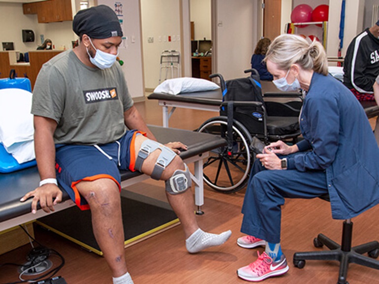 Male patient wearing a knee brace and sitting on a therapy table to practice flexing his foot.
