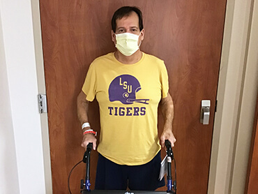 A male patient wearing a yellow shirt standing at the door to a hospital room.