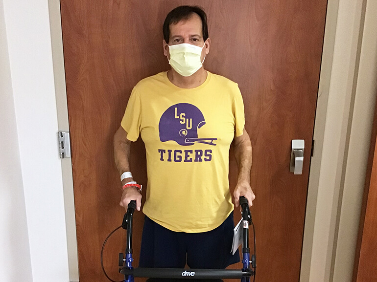 Darren wearing a yellow hospital mask and matching yellow shirt, standing outside a hospital room doorway.
