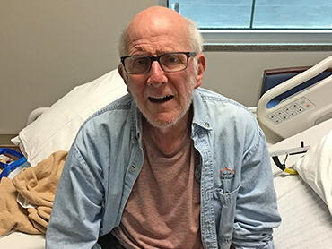 Patient Harry Vorhaben sitting up on the edge of his hospital bed after recovering from a hip fracture.