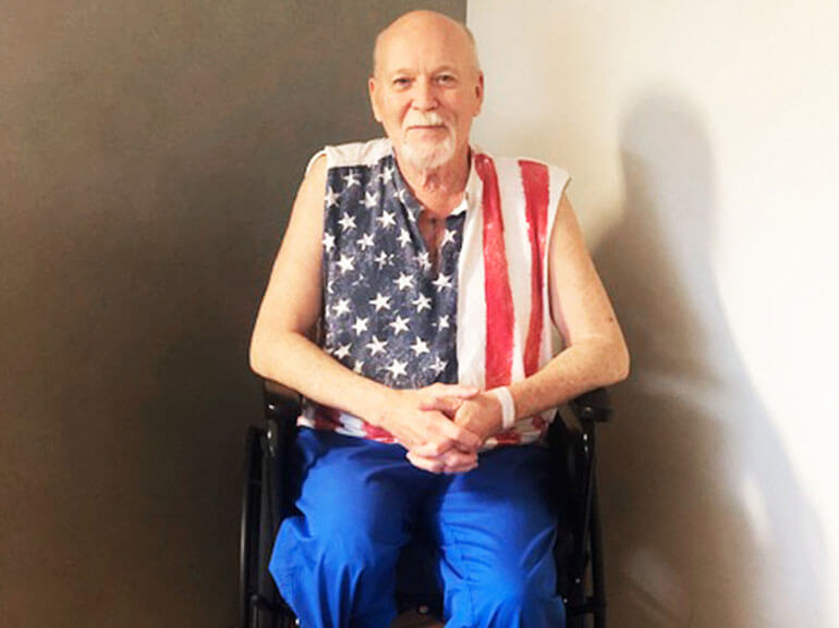 Bernie wearing a sleeveless American flag shirt and sitting in a wheelchair.