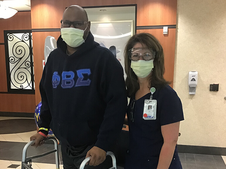 Dramar wearing a Phi Beta Sigma sweatshirt and standing with a walker in the hospital lobby.