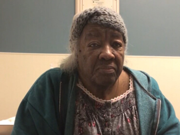 Woman wearing a gray crocheted head band, sitting in a hospital room.