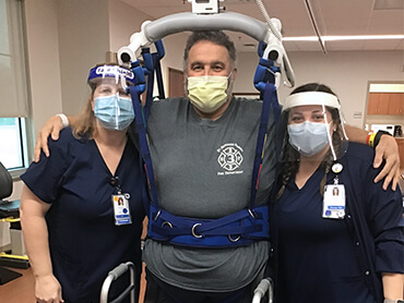 Man in an overhead safety harness standing between two therapists with his arms wrapped around their shoulders.