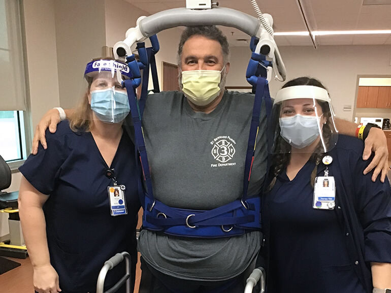Rory standing with his walker with his arms around two therapists. 