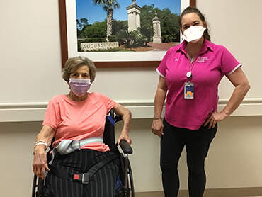 Physical therapist standing next to a woman with gray hair sitting in a wheelchair.