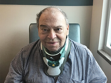 Older man wearing a cervical neck brace and sitting in a hospital room.