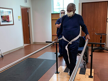 Male patient holding onto parallel bars to practice walking.