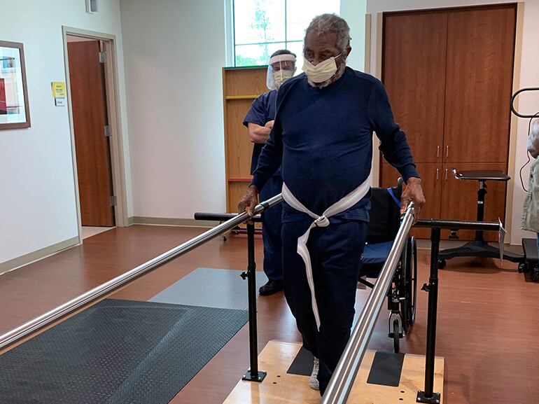 Alex walking between parallel bars during a therapy session.