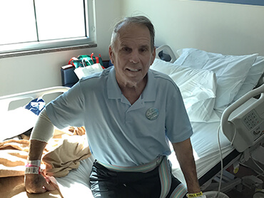 Male patient  with white hair sitting on the side of his hospital bed.