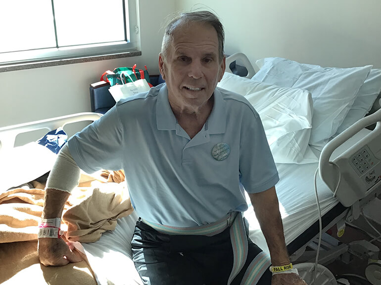Gaston wearing a light blue shirt and sitting at the edge of his hospital bed.