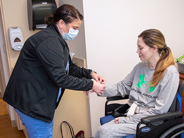 A nurse placing a hospital identification bracelet on the wrist of a young woman in a wheelchair.