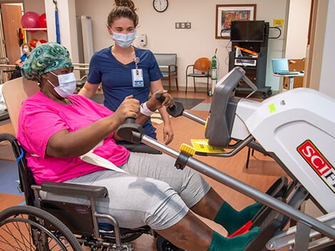Woman using a total body exerciser in a therapy gym to build endurance.